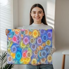 a woman holding up a colorful painting with circles in the center on it's canvas