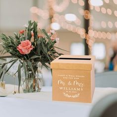 a vase with flowers on top of a table in front of a box that says our wedding date