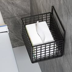 a black wire basket holding napkins and papers in a gray tiled room with grey walls