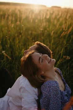 a woman laying on top of a lush green field next to a man in a white shirt