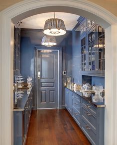 an archway leads into a kitchen with blue cabinets and wood floors, along with a chandelier hanging from the ceiling