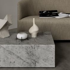 a marble coffee table with two vases on it next to a couch and magazine rack