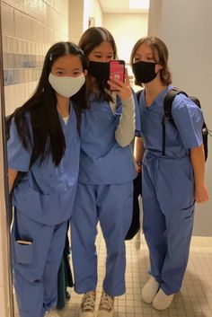 three women in scrubs are taking a selfie with their cell phone while wearing masks