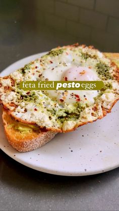 a piece of bread with an egg in it sitting on a plate that says feta fried pesto eggs