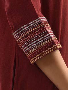 a woman's arm wearing a red shirt with an intricate design on it and a striped cuff