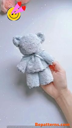 a hand holding a small gray teddy bear