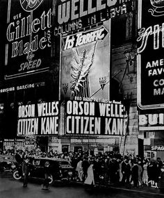 an old black and white photo of people walking on the street in front of advertisements