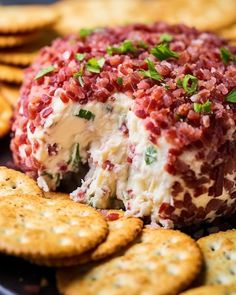 a cheese ball covered in red and white toppings next to crackers on a black plate