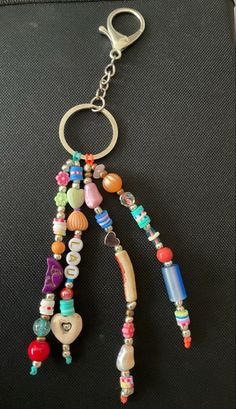 a bunch of beads hanging from a metal hook on a black surface with a keychain attached to it