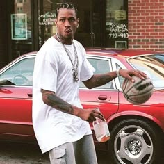 a man holding a basketball in front of a red car