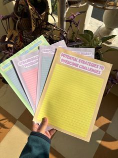 a person holding four notebooks with writing on them in front of some potted plants