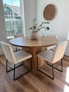 a round wooden table with four chairs around it and a vase on the table top