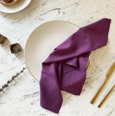 a purple napkin sits on a white plate next to gold utensils