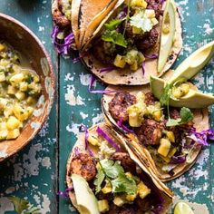 three tacos with meat and vegetables on them next to a bowl of guacamole