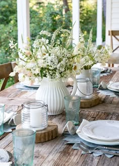 a wooden table topped with vases filled with white flowers and greenery on top of it