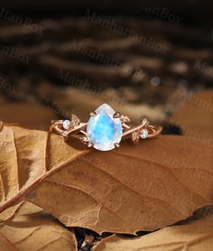 an oval blue stone surrounded by white diamonds sits on top of a leaf in the sun