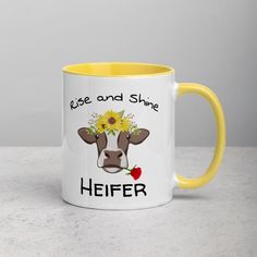 a yellow and white coffee mug that says rise and shine heifer with a cow's face on it