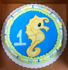 a blue and yellow birthday cake with a sea horse on the top is in a cardboard box