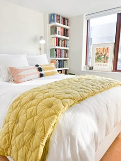 a bed with yellow and white comforter in front of a book shelf filled with books