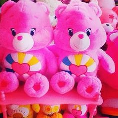 two pink teddy bears sitting on top of a shelf filled with other stuffed animals and toys