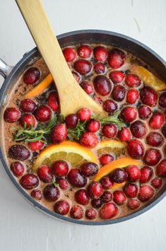 a pan filled with berries and oranges on top of a white table next to a wooden spoon