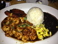 a white plate topped with shrimp, rice and other foods on top of a wooden table