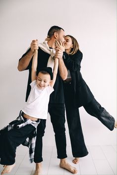 a man, woman and child standing in front of a white wall with their hands on each other's shoulders