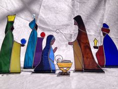 four stained glass nativity figurines are lined up on a white cloth background