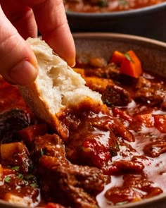 a person dipping bread into a bowl of stew