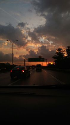 the sun is setting behind some cars on the road