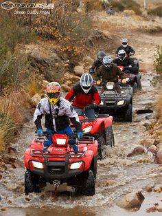 four people on four wheelers in the water