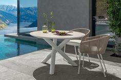 a table with two chairs next to a pool and mountains in the backround