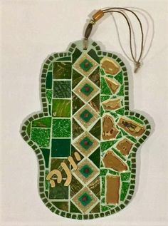 a hamsa hanging on the wall with green and brown mosaic tiles in it's center