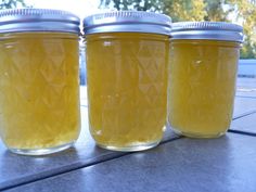 three jars filled with yellow liquid sitting on top of a cement floor next to trees