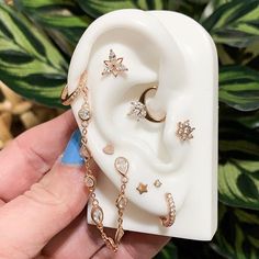 a person holding a fake ear with some jewelry attached to it and a plant in the background