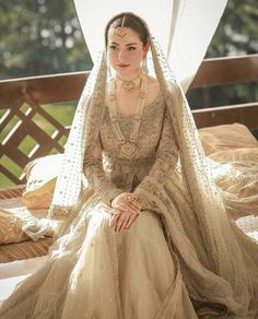 a woman sitting on top of a bed wearing a dress and headpiece with pearls