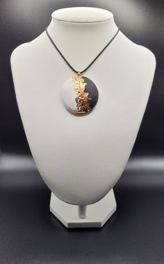 a necklace with a black and gold pendant hanging from it's side on a white mannequin