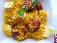 a white plate topped with yellow rice and meat covered in sauce, garnished with cilantro