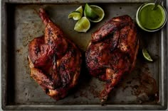 two pieces of chicken on a baking sheet with limes and cilantro sauce