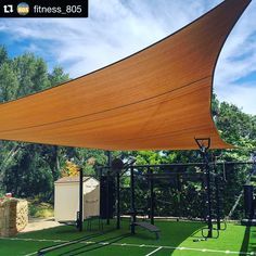 a large shade structure in the middle of a grassy area with trees and bushes behind it