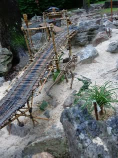 there is a miniature train set on display in the sand with rocks and trees around it