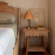 a small wooden table with a lamp on it next to a neatly made bed in a bedroom