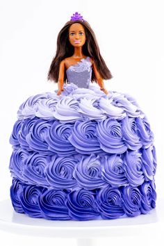 a doll sitting on top of a purple cake with icing curls in the shape of a ball gown