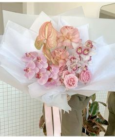 a bouquet of pink and white flowers is held up by someone's hand in front of a tiled wall