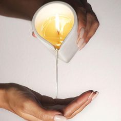 two hands holding a white container with yellow liquid pouring from it into the palm of another hand