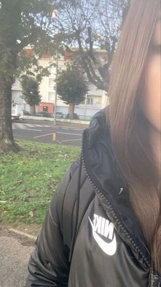 a woman with long brown hair standing in front of a tree wearing a nike jacket