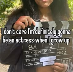 a woman holding a clap board with the words i don't care i'm definitely going to be an actress when i grow up