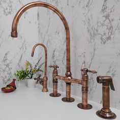 two faucets are next to each other on a white countertop in front of a marble wall