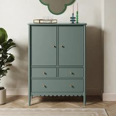 a green cabinet with two drawers and a mirror on top of it next to a potted plant