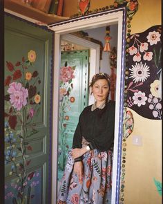 a woman standing in front of a doorway with flowers painted on it